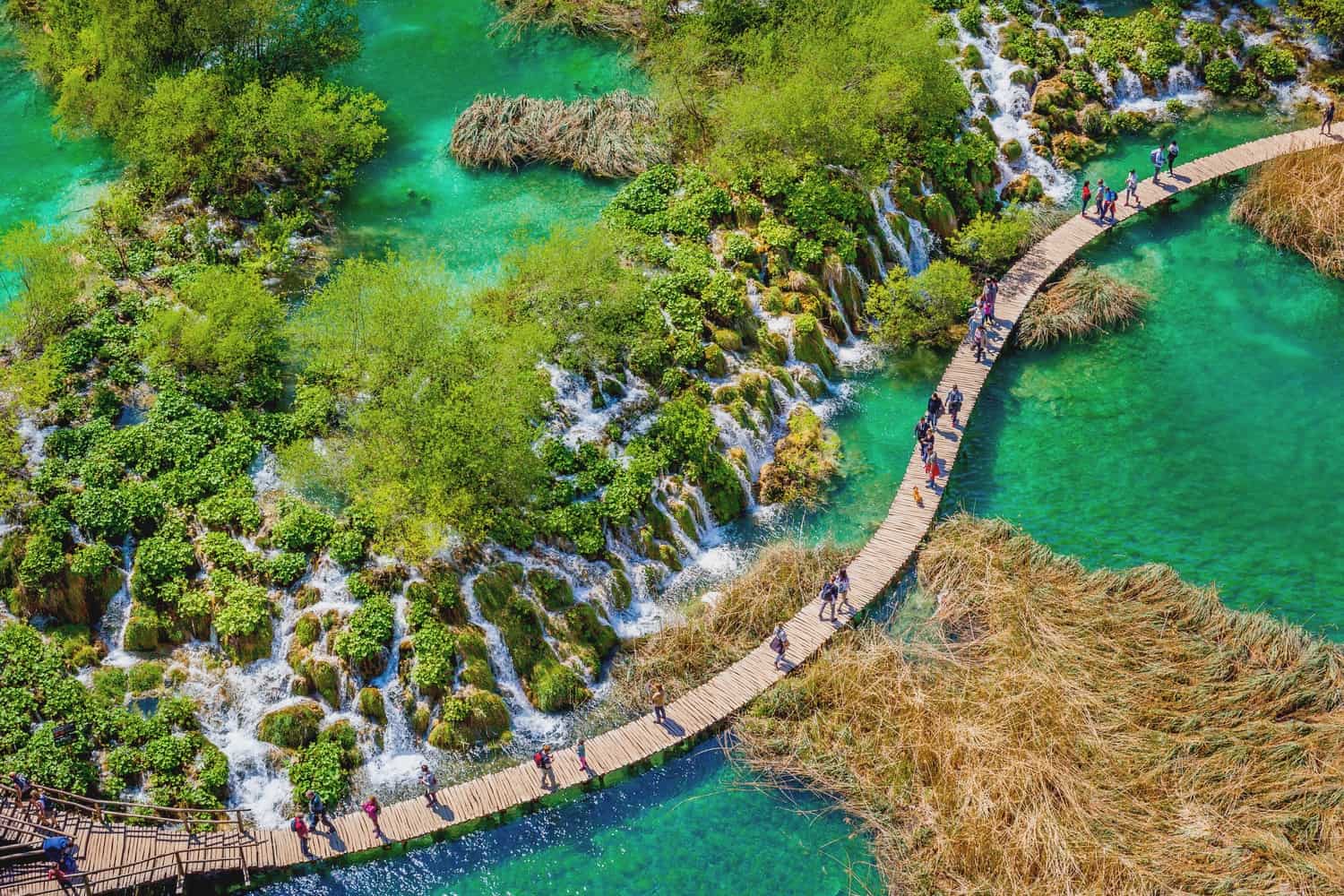 Plitvice Lakes from above with people on the walkway. Many small waterfalls are visible alongside the walkway.