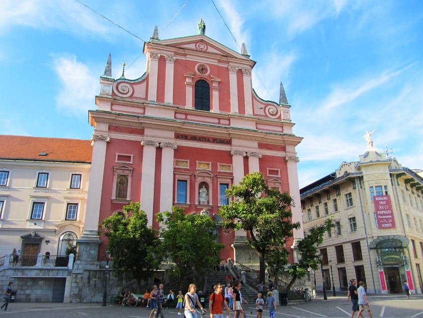 Tall pink building on a city street, with religious statues and artwork on the top and sides. 