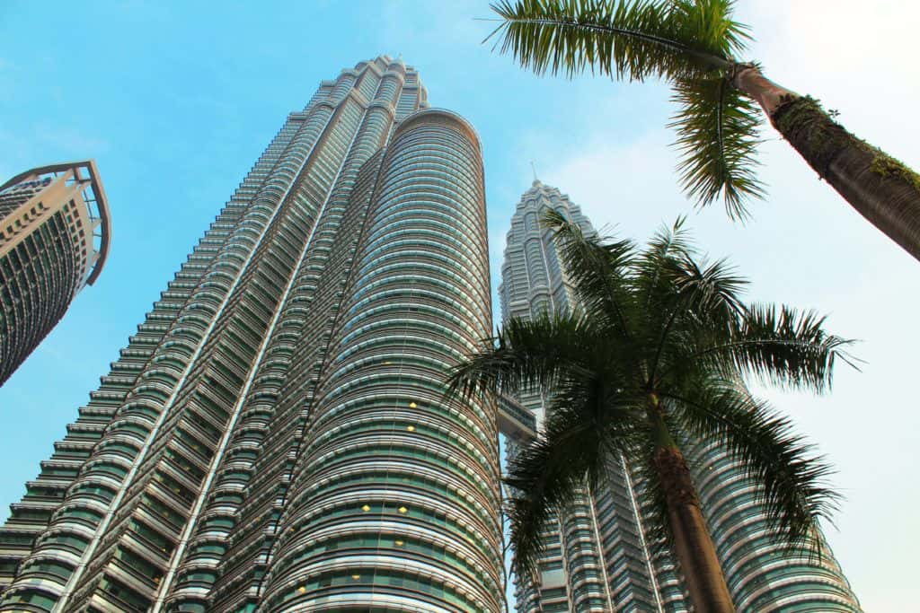 Looking up at two tall, near-identical buildings alongside each other, with two palm trees alongside and a third, different style of tall building partially visible.