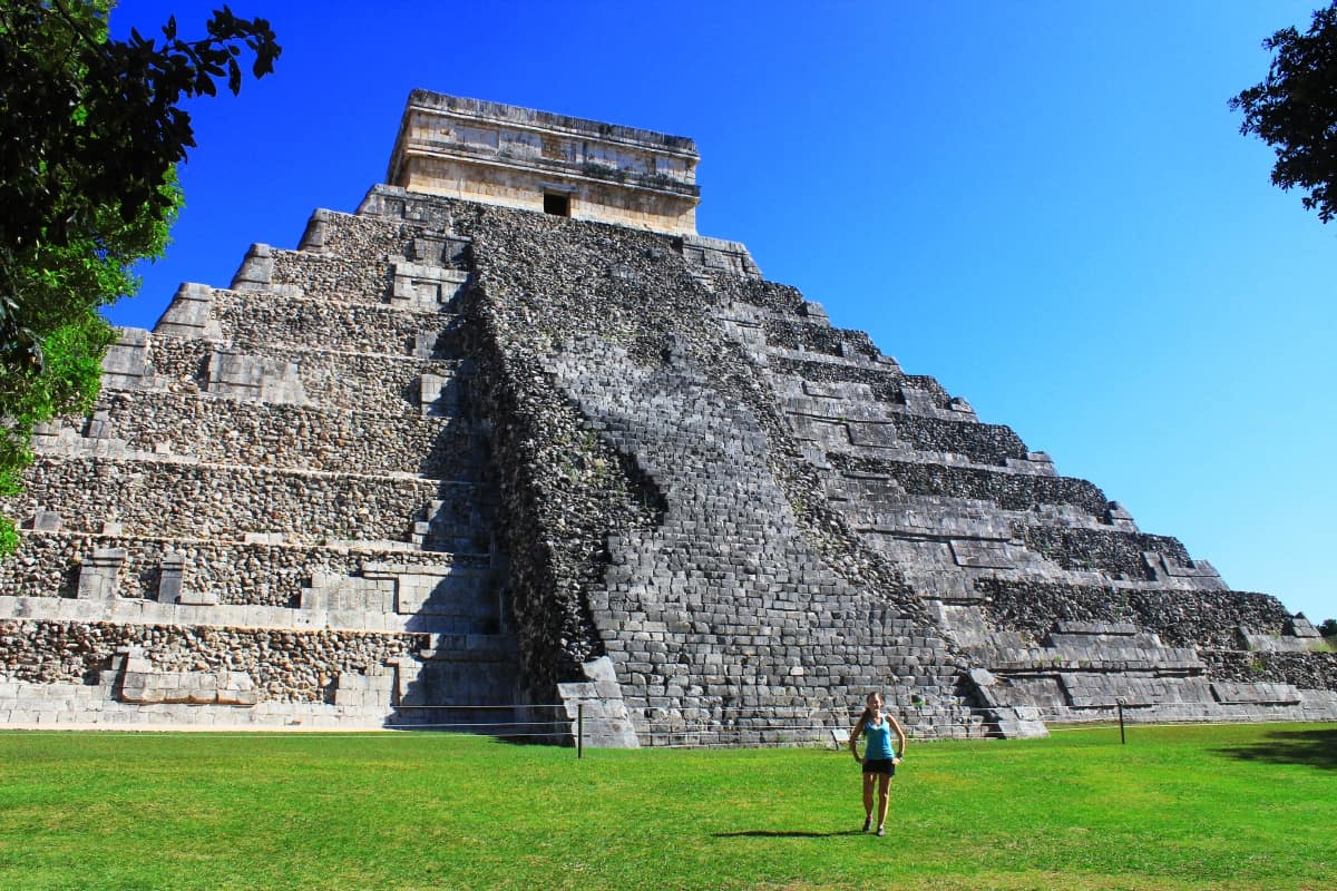 Woman standing on grass in front of a large stone structure at Chichen Itza in Mexico.