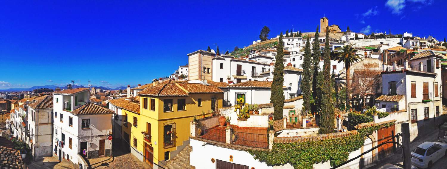 Panoramic view of predominantly orange and white houses on a hillside in Granada, Spain, with mountains faintly visible in the background