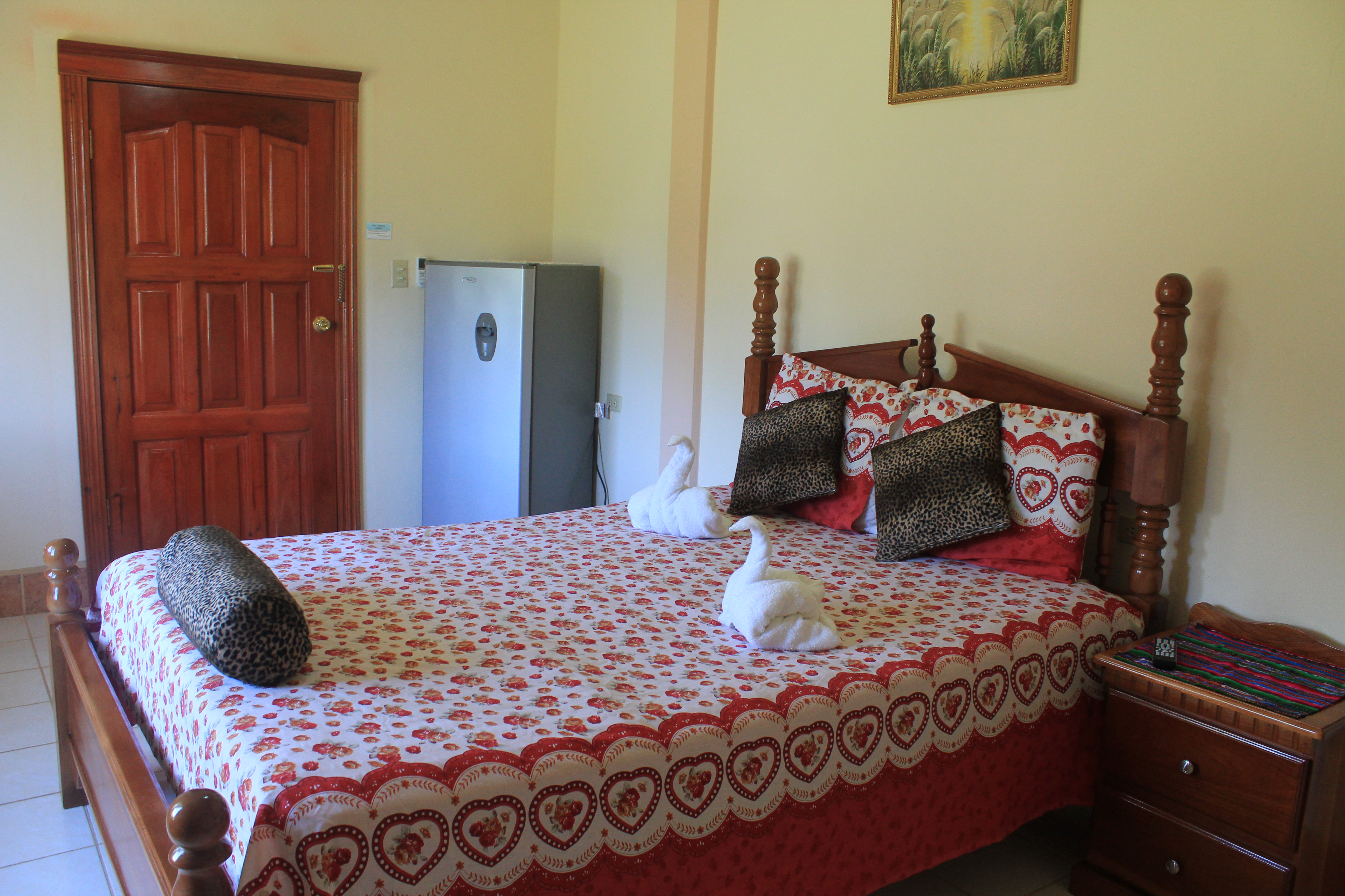 A simple guesthouse room in Belize, with a bed, small set of drawers, and a fridge.