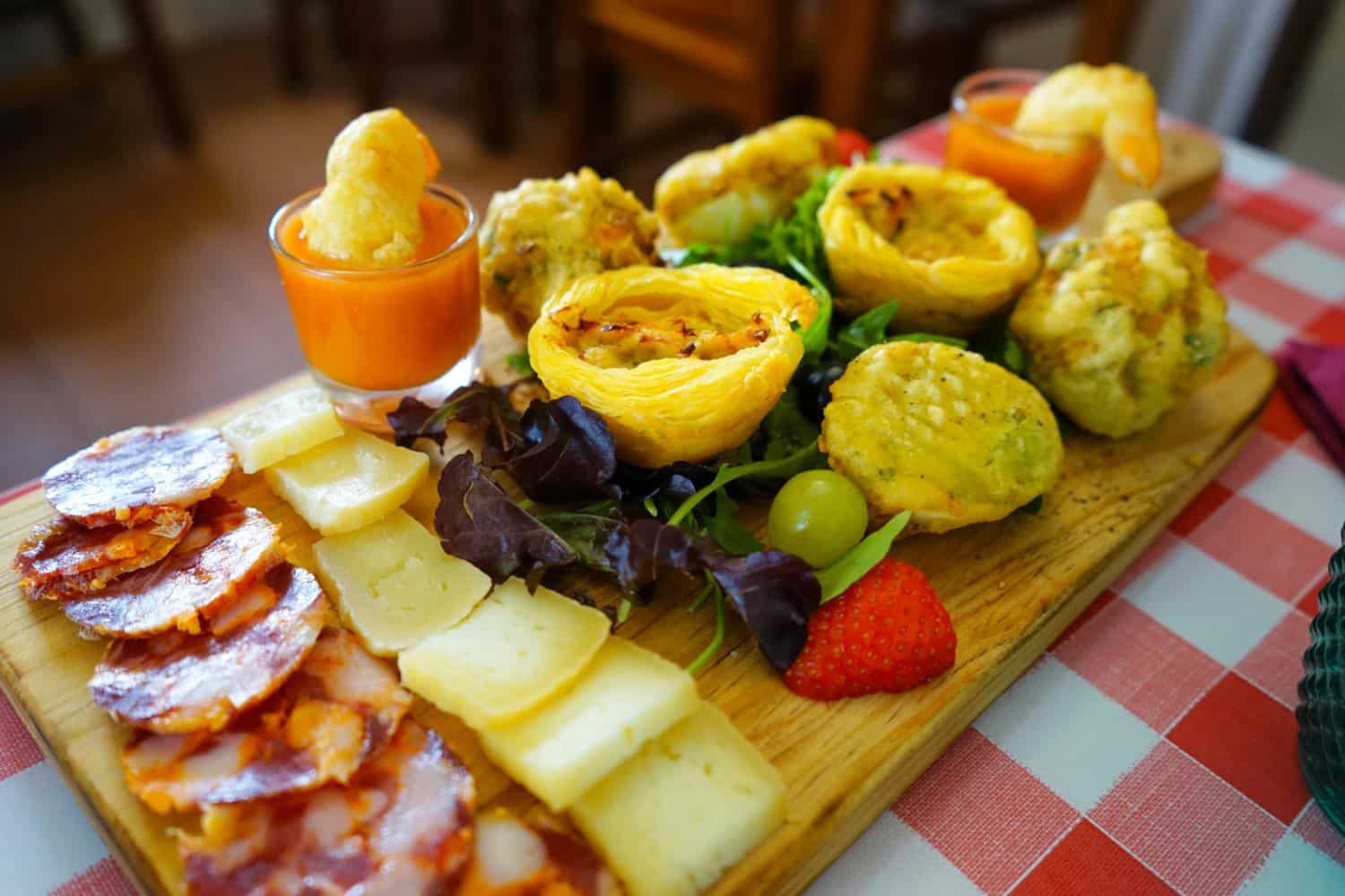 Meat, cheese, pastries, and fruit on a wooden tasting platter, sitting on a checked tablecloth
