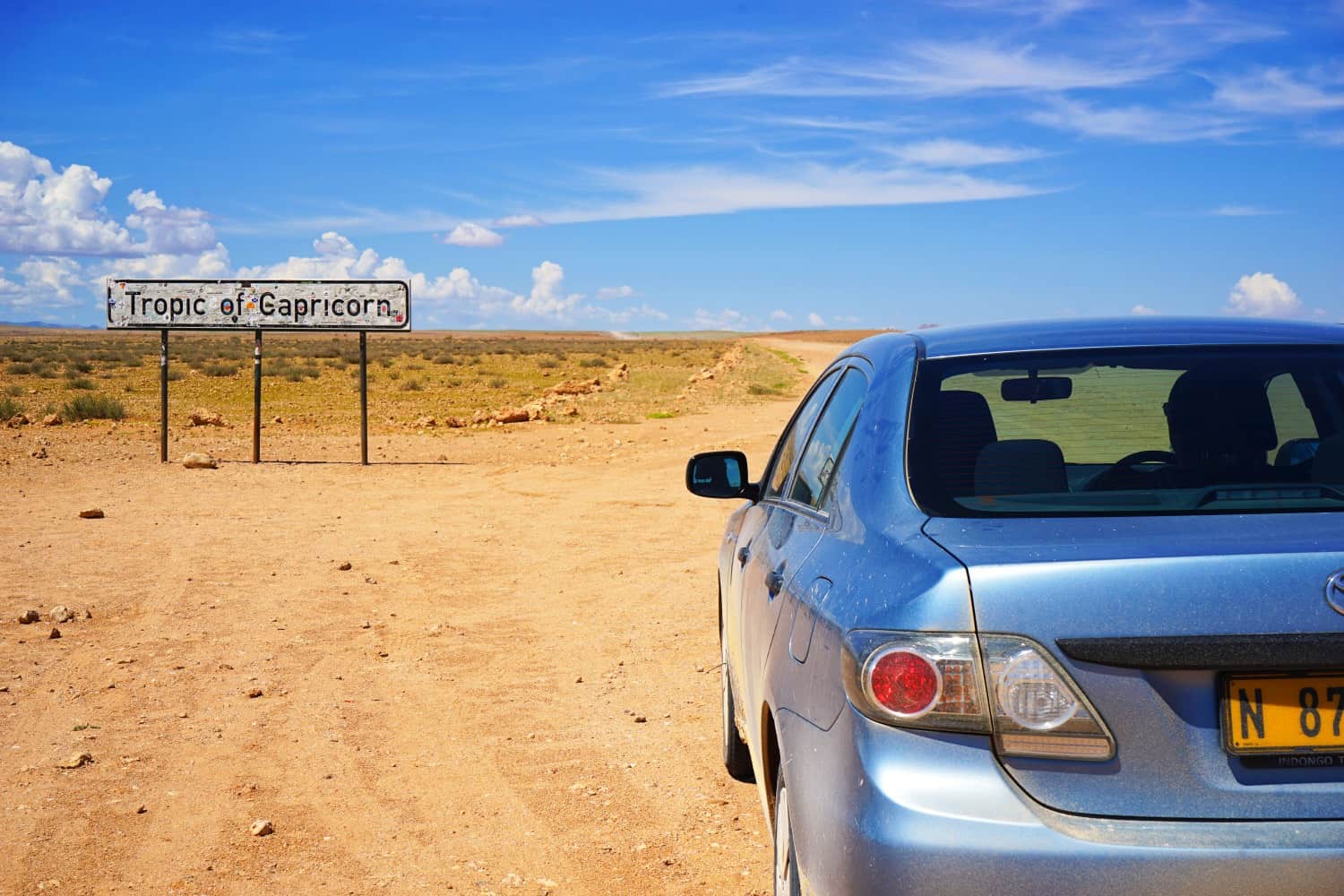 Dusty card parked on the side of a dirt road with a sign saying "Tropic of Capricorn" in front