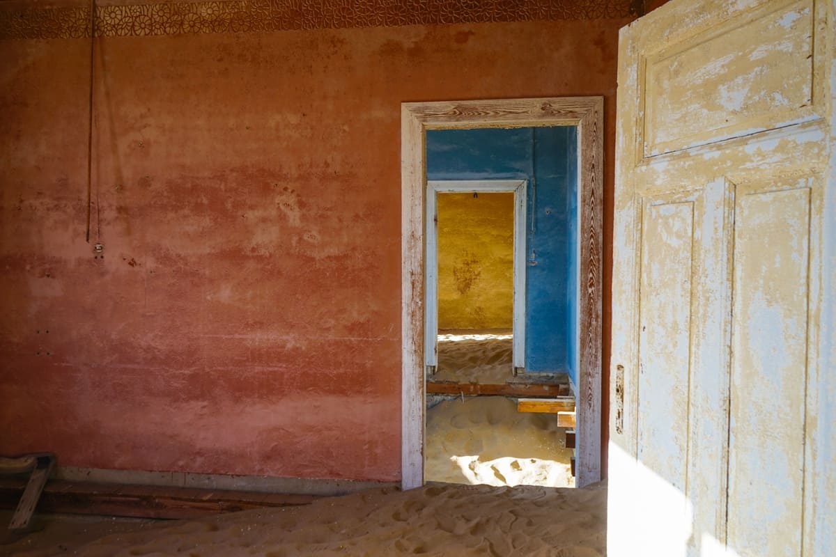 A series of rooms at Kolmanskop with different paint colours on the wall. The colours transition from red to blue to yellow. 