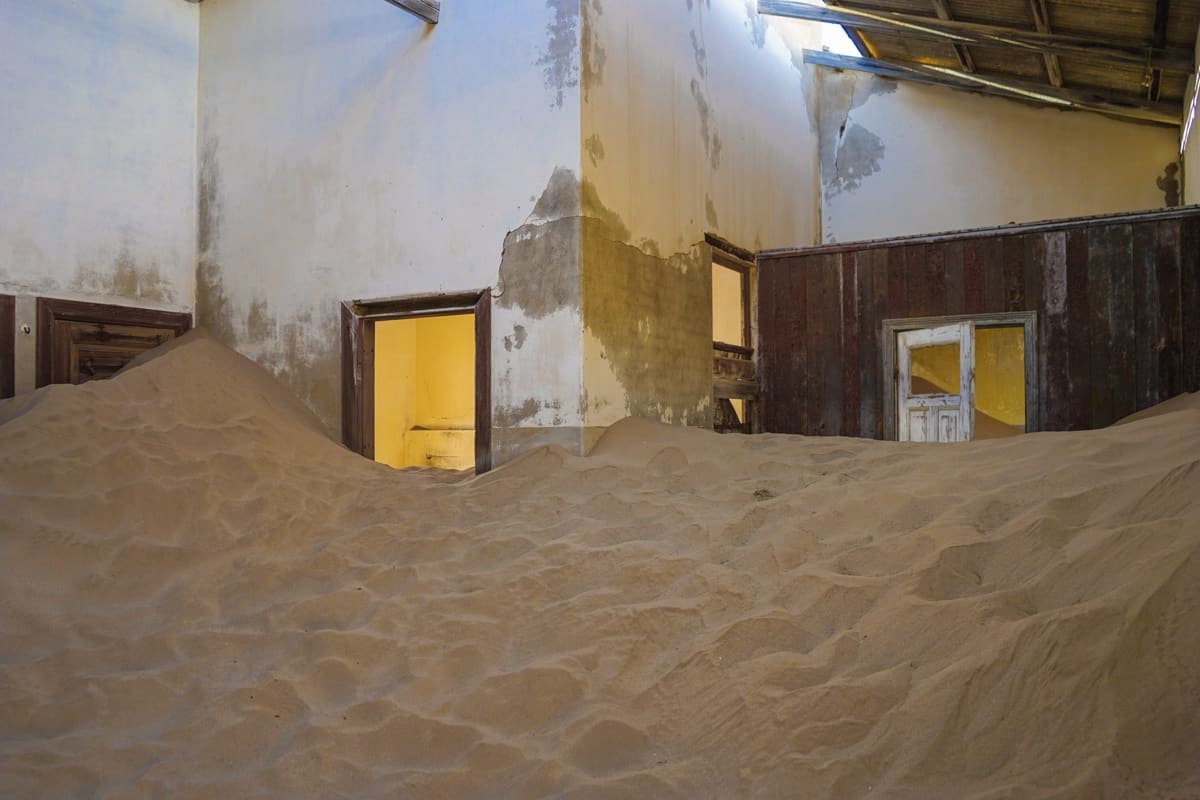 A white room that's filled with sand. There's so much that it's reaching the top of the door frames at points.
