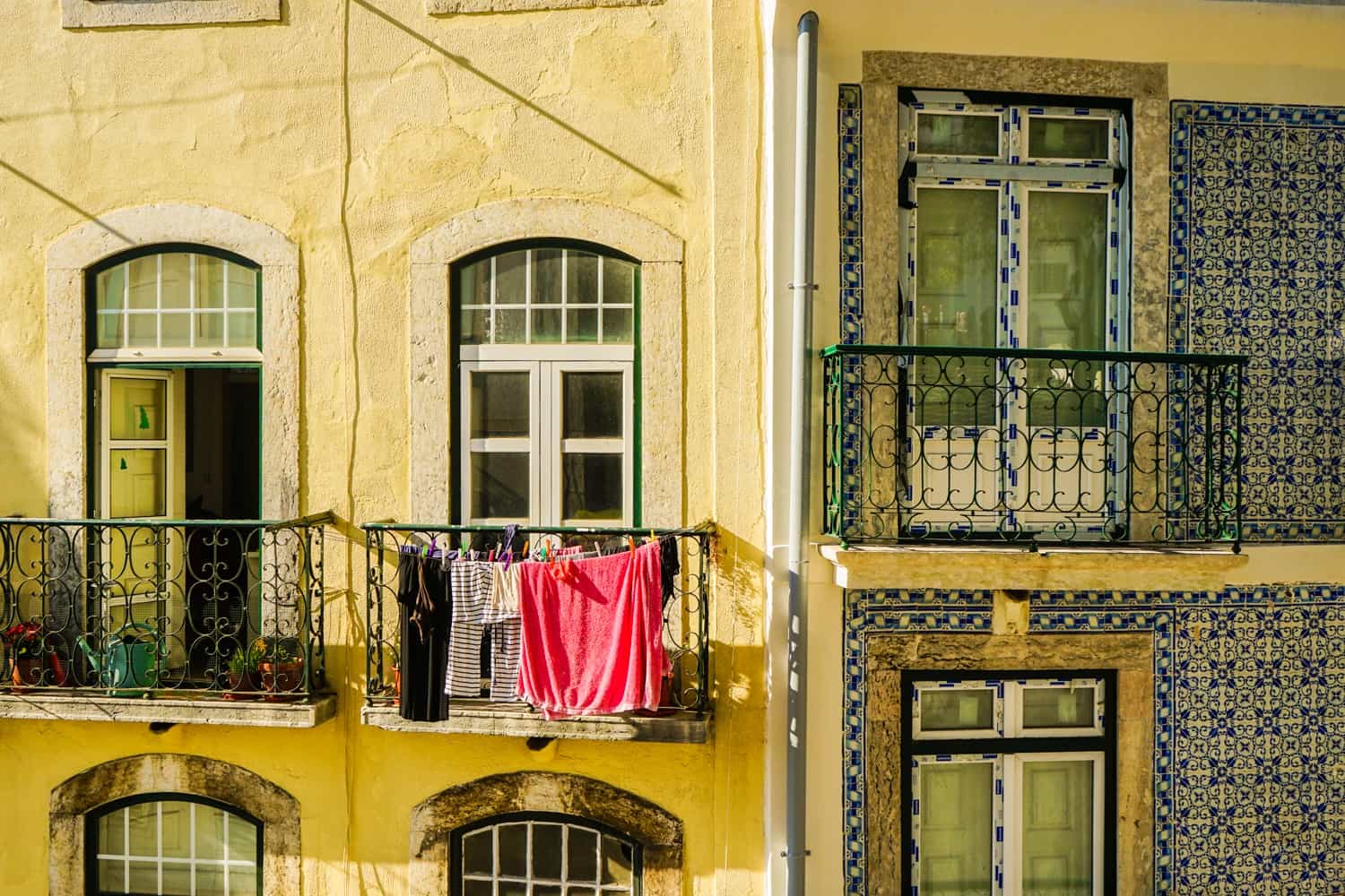 Close-up of the corner of a house in Lisbon, with brightly-coloured tiles on part of one wall, and washing hanging on one of the balconies