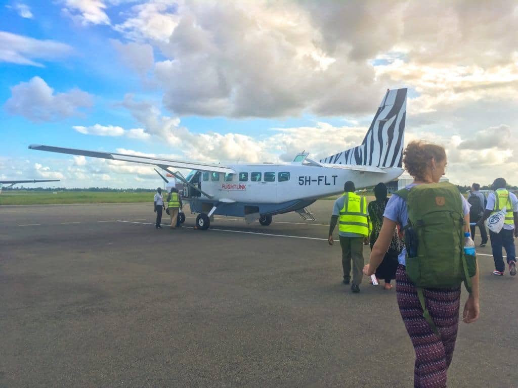 A small propeller plane parked on a runway, with several people walking towards it.