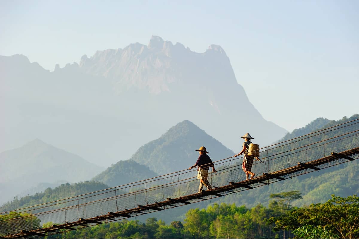 Two farmers walking across a wooden suspension bridge in Borneo