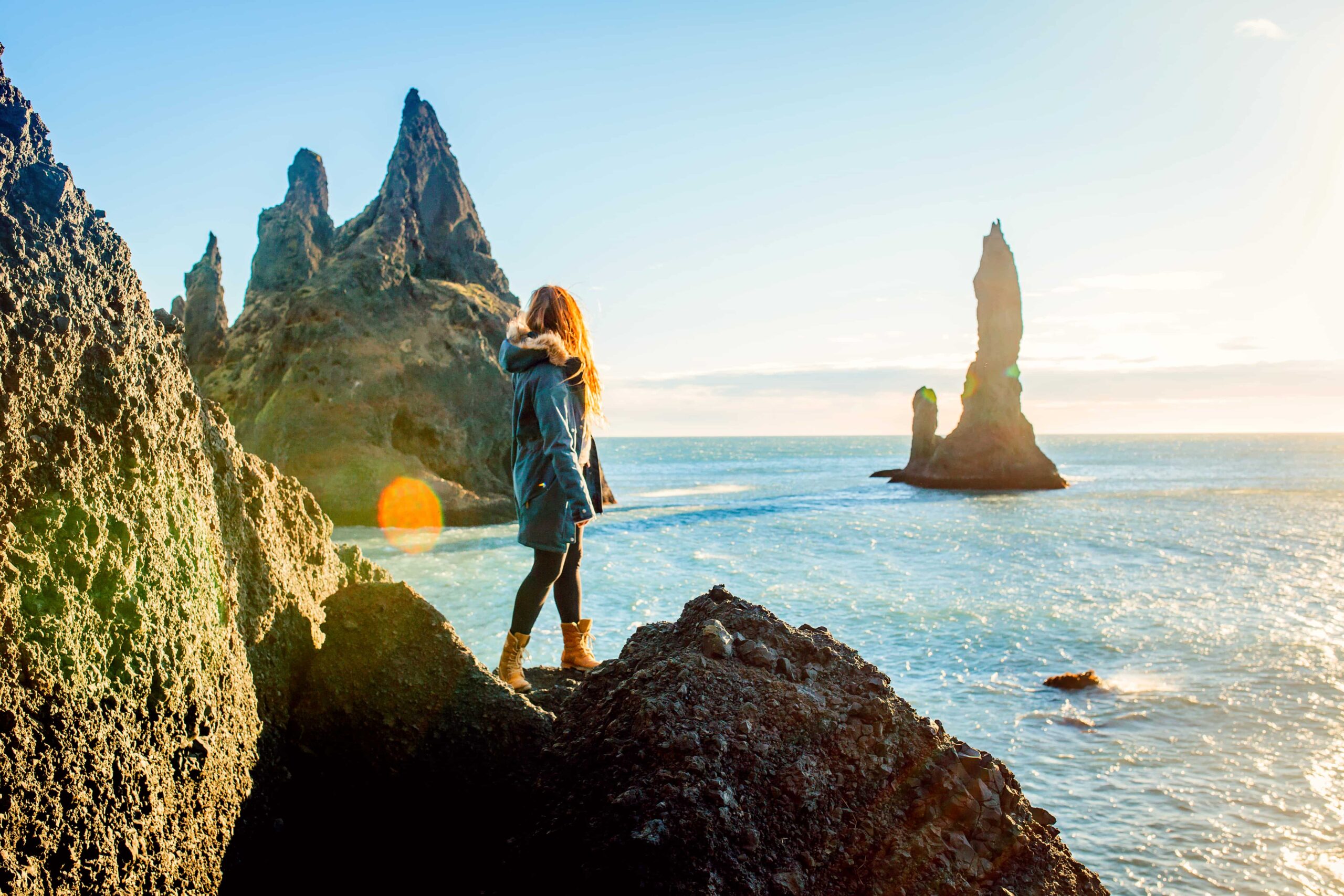 Woman standing on a rocky outcrop looking out at similar jagged rocks in the ocean nearby.
