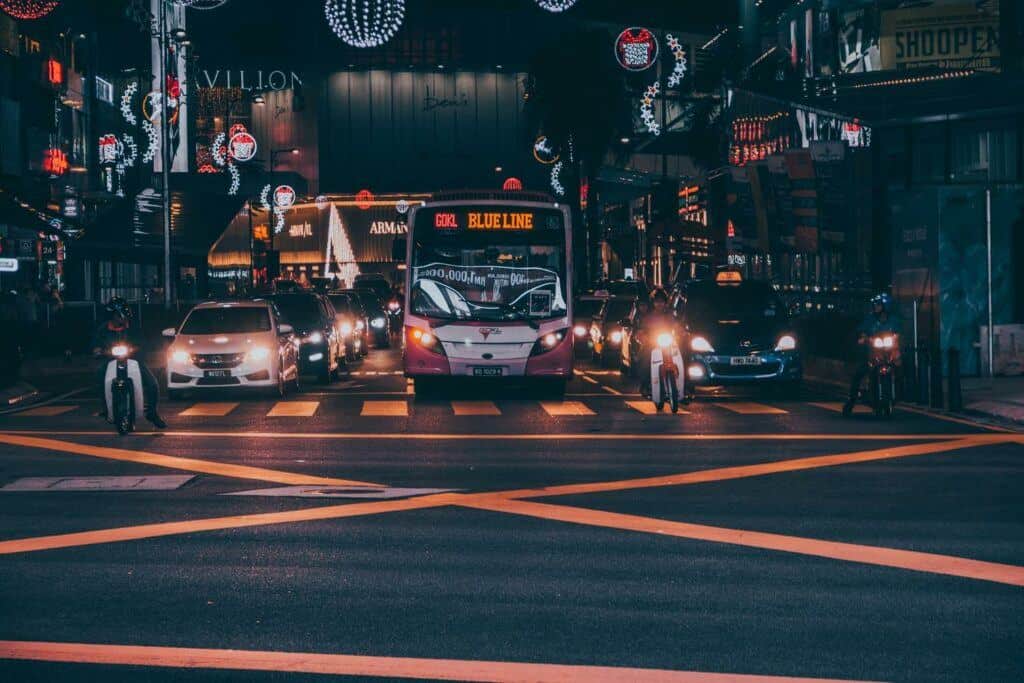 Bus, private cars, taxis, and motorbikes stopped at an intersection in Malaysia at night.