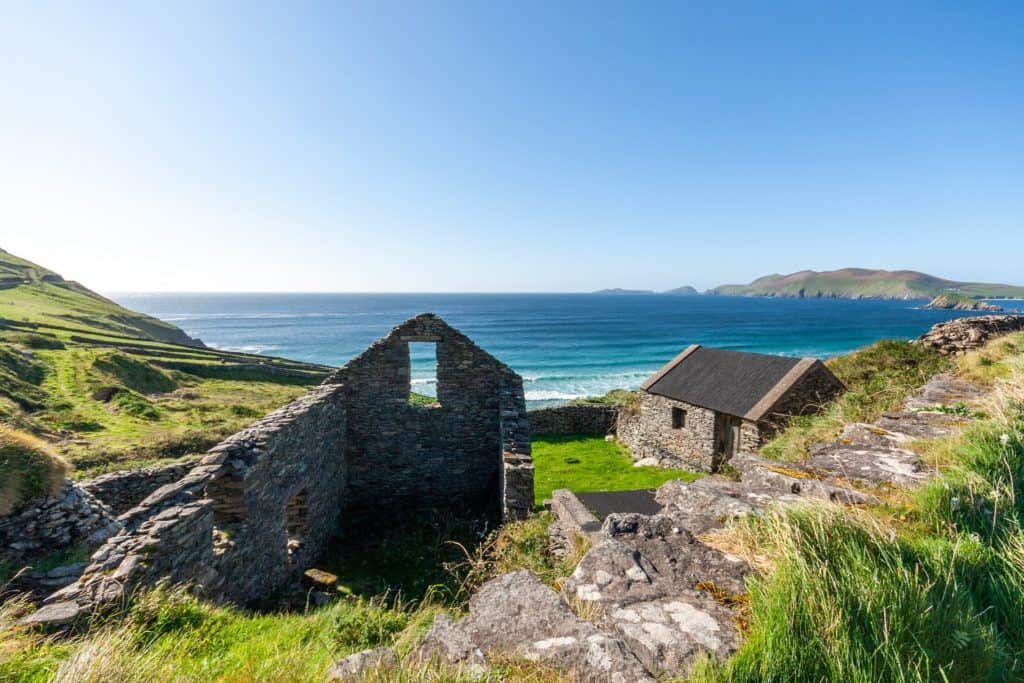 Ruined stone building on a cliff overlooking the ocean, with another non-ruined stone building nearby.