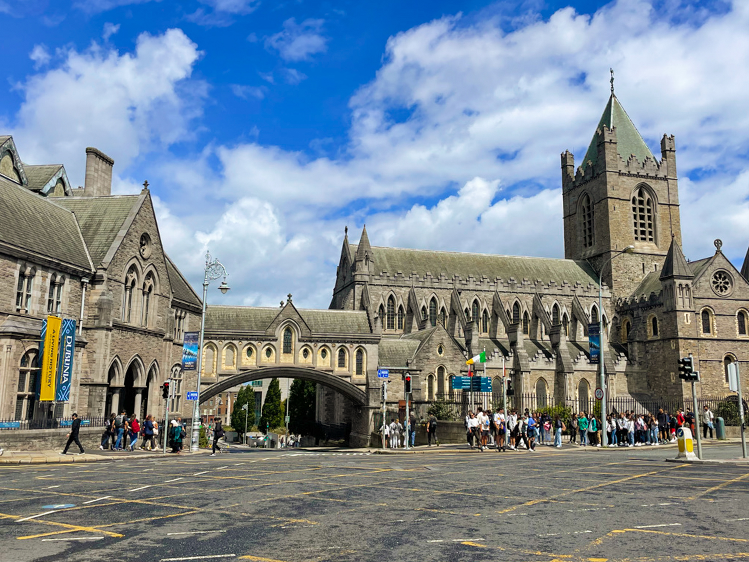 The old-looking Christ Church cathedral beside a major road. A covered stone bridge archway links the cathedral over a smaller road, allowing pedestrians to pass over top of it.