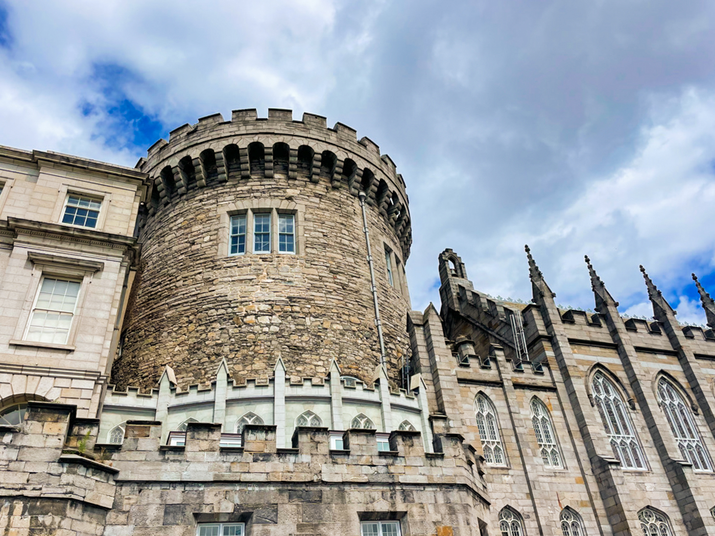 The grey stone turret of Dublin Castle peeks out through the middle of the surrounding brick buildings. Overhead, patches of blue peek out through the dense clouds in the sky.